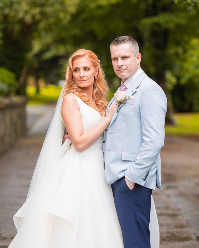 Bride glancing over her shoulder with her hand on the groom&rsquo;s chest while he looks at the camera, golden hour in the gardens of Greenway Manor Hotel