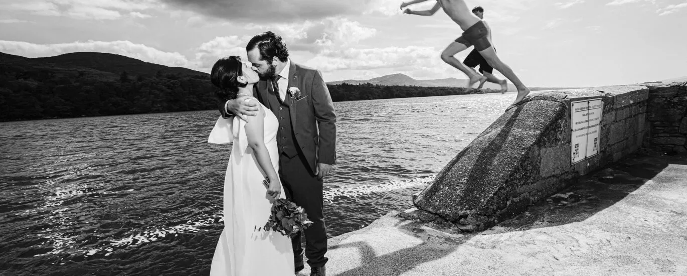 A passionate Kiss at kenmare bay while school children leap into the water JODPhotography