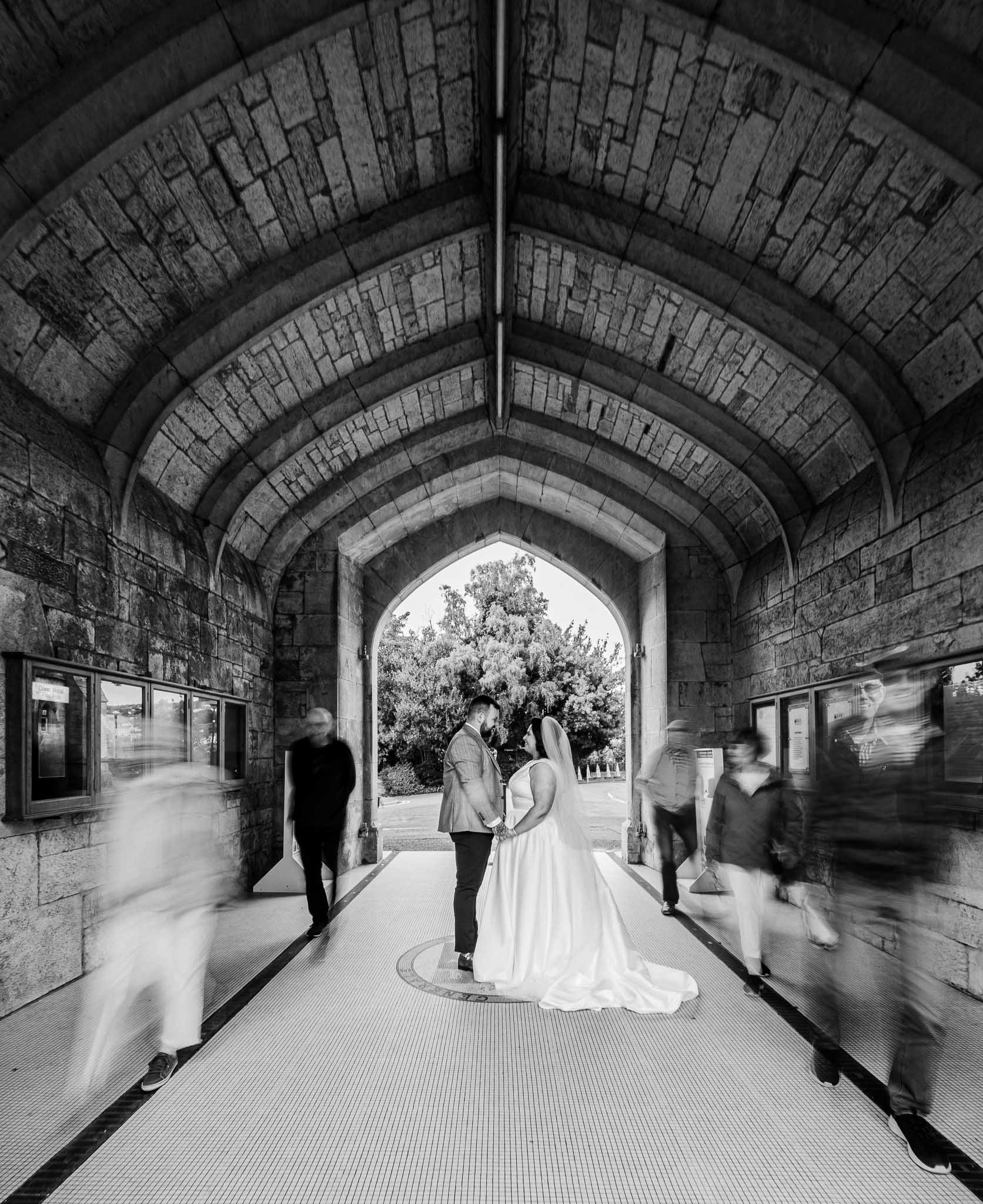 Bride and groom holding each other tightly in university College Cork as people walk by in blur. Creative Photography Cork