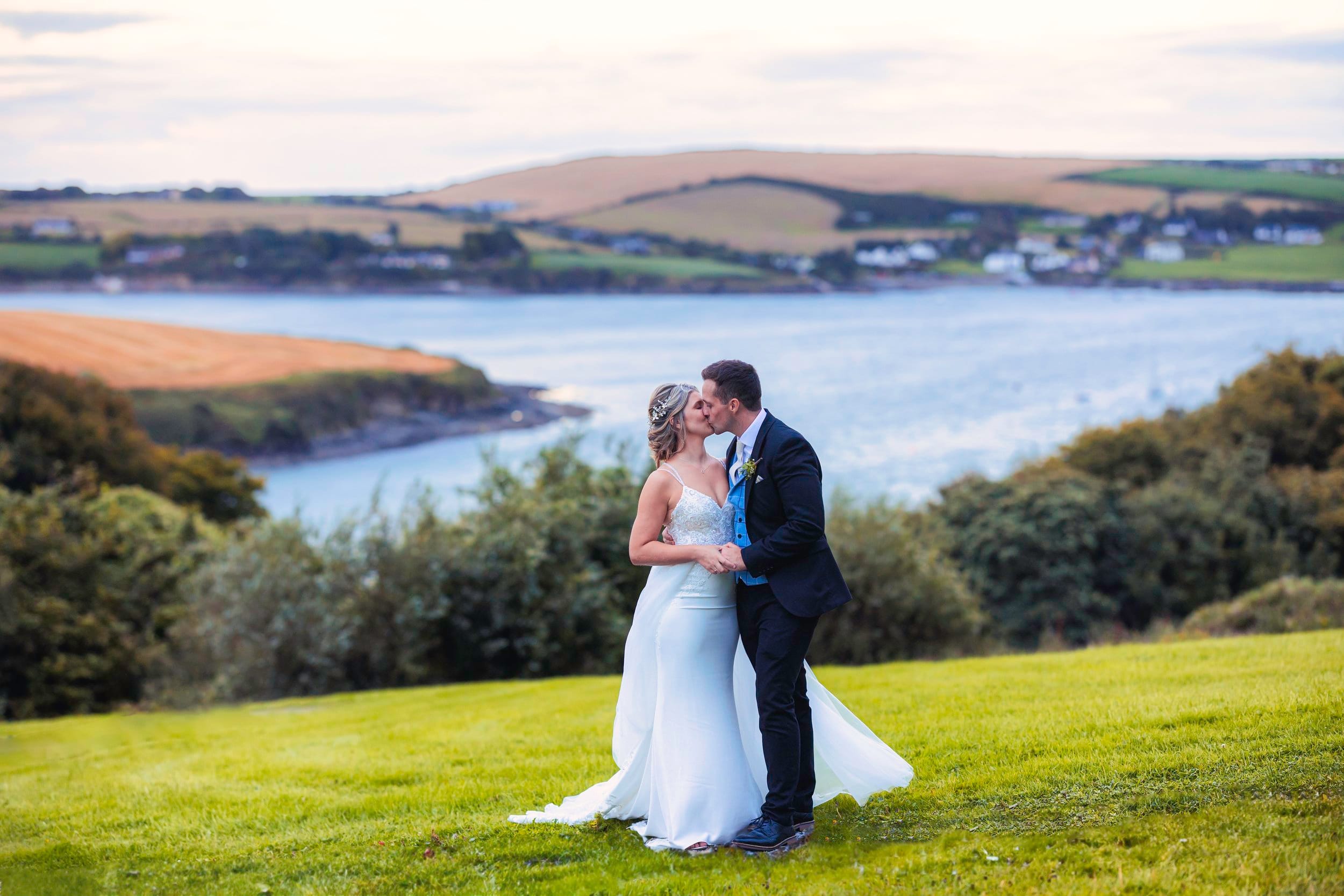 Bride and groom share a kiss with Kinsale stunning landscape behind them at sunset - JOD'Photography