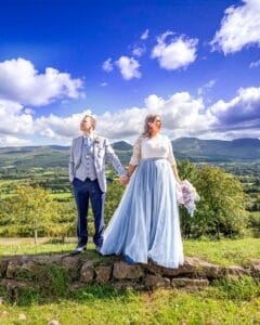 Bride and groom standing below Limerick Mountains on super sunny blue sky day-JOD'Photography