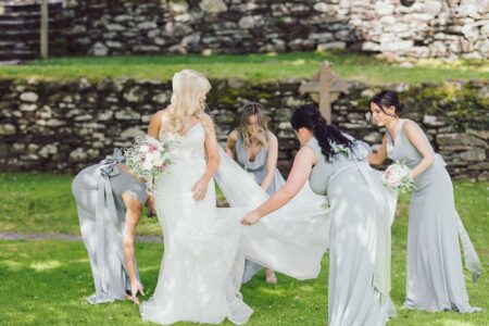 Bridesmaid fixing brides dress outside Gougane barra Church Cork on a beautiful sunny day