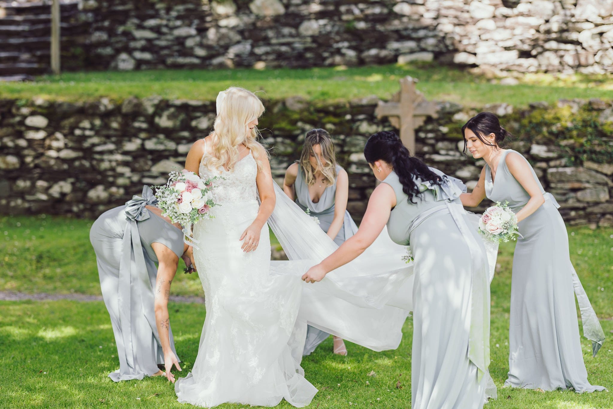 Bridesmaid fixing brides dress outside Gougane barra Church Cork on a beautiful sunny day
