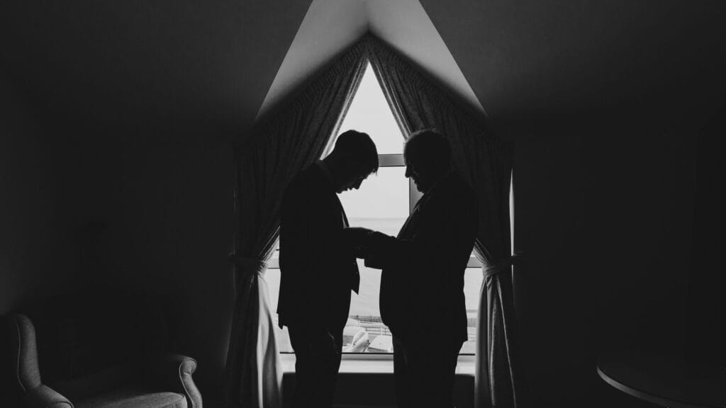 Father helping sin into his suit by the window light in Dumore house hotel west cork