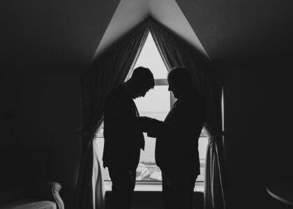Father helping sin into his suit by the window light in Dumore house hotel west cork