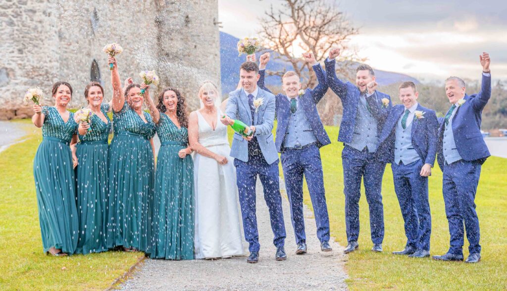 Groom shakes and sprays champagne everywhere at Ross castle in Killarney Co Kerry as bridal party cheer and raise their hands