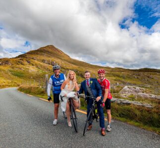 Local Cyclist stop to help create a fun wedding portrait for the bride and groom as they stop on the road by Molls Gap Kenmare Co Kerry