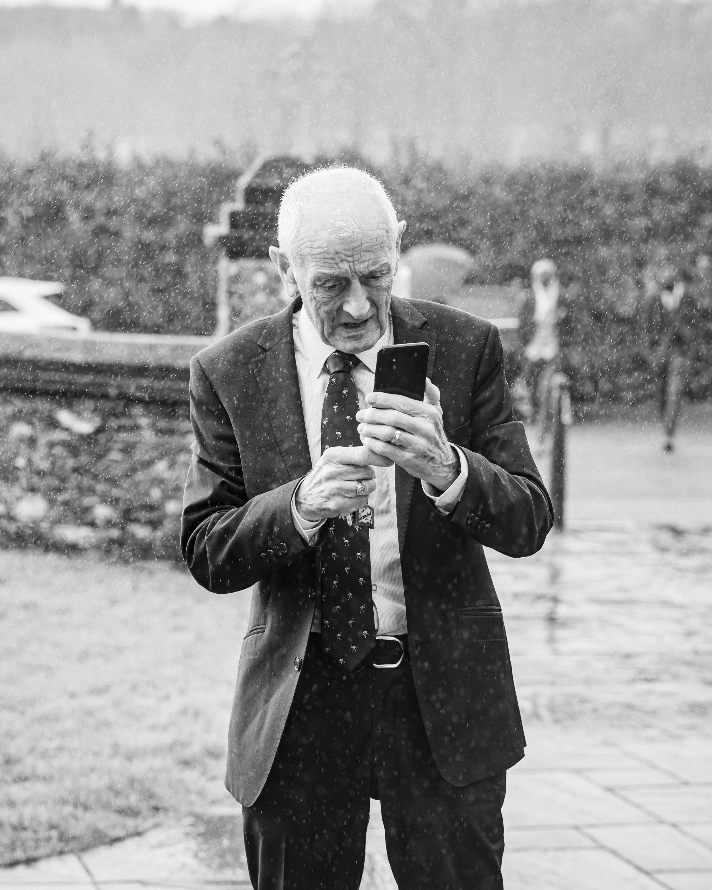 Old man standing in the rain in west Cork checking his phone
