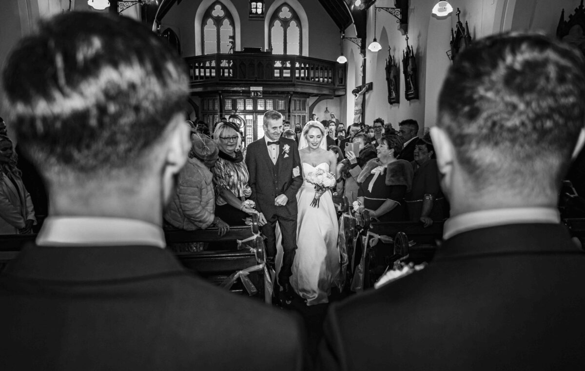 The groom and best man watch on as the bride and her father walk down the aisle in a church on Valentia island Co Kerry