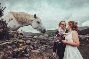West Cork a wild horse comes to greet a bride and groom with the Irish rugged Landscape behind them