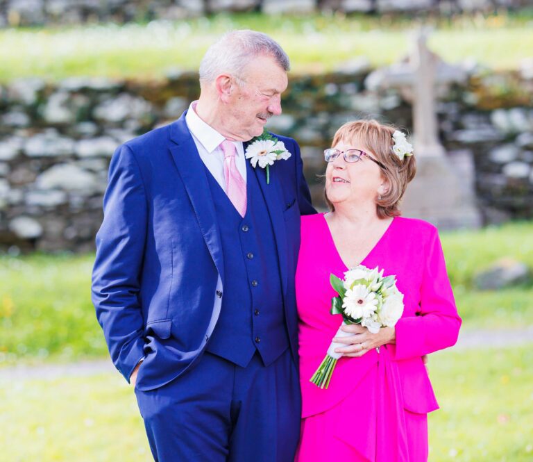 Smiling couple in the grounds at Gougane Barra with the old stone cross behind them