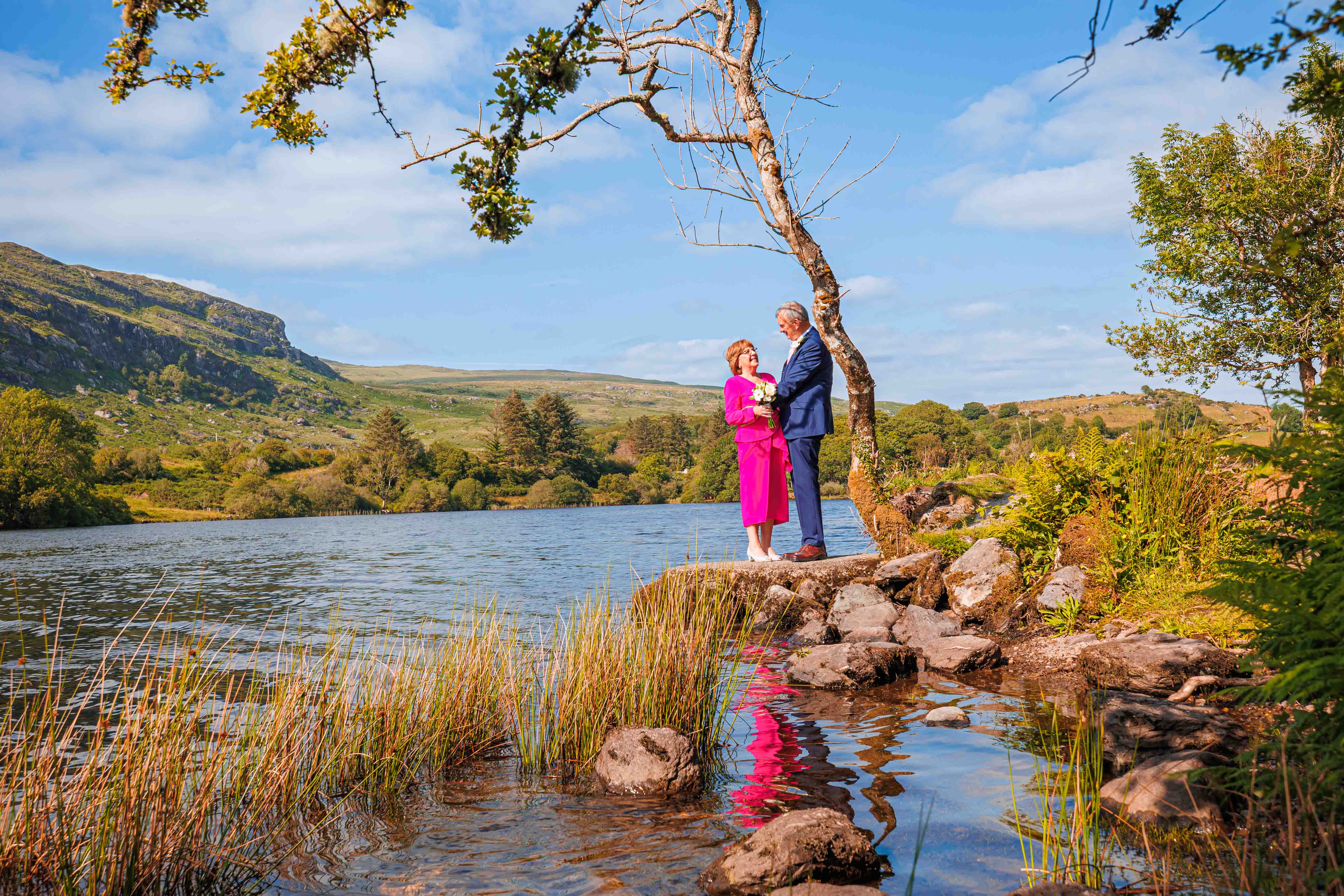 Bride walking toward Gougane Barra chapel in soft purple dress – JOD'Photography