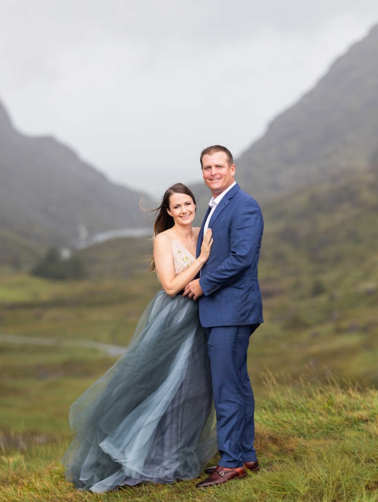 Couple looking at the camera in the Gap of Dunloe mountains, bride in a grey-blue tulle dress and groom in a blue suit, Co. Kerry