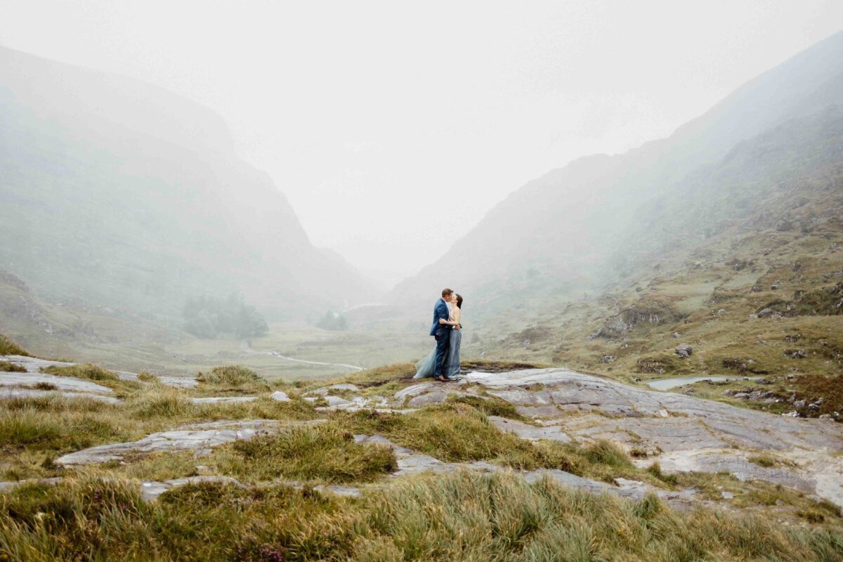 Tiny couple embracing on a rocky ledge in the misty Gap of Dunloe valley, Killarney