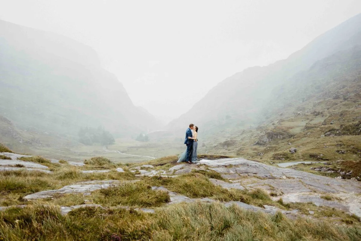Tiny couple embracing on a rocky ledge in the misty Gap of Dunloe valley, Killarney