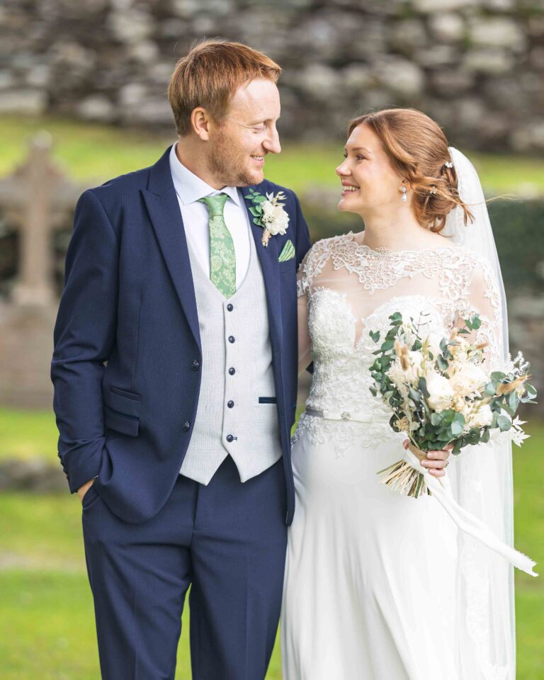 Groom and bride smiling at each other in the grounds at Gougane Barra, West Cork