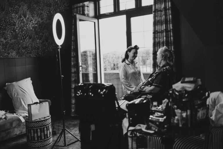 Black and white behind-the-scenes photo of a bride getting ready beside a ring light