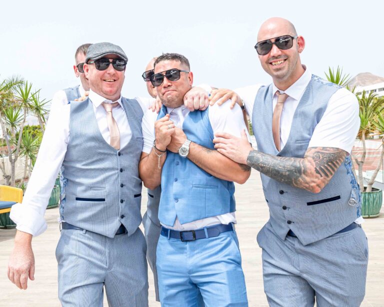 Groom and groomsmen in sunglasses laughing with their arms around each other