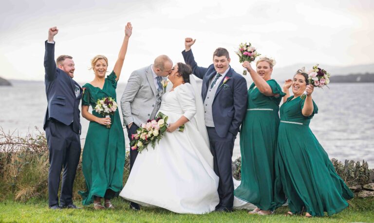 Bride, groom and bridesmaids in green dresses cheering on the shore in Kenmare, Co. Kerry