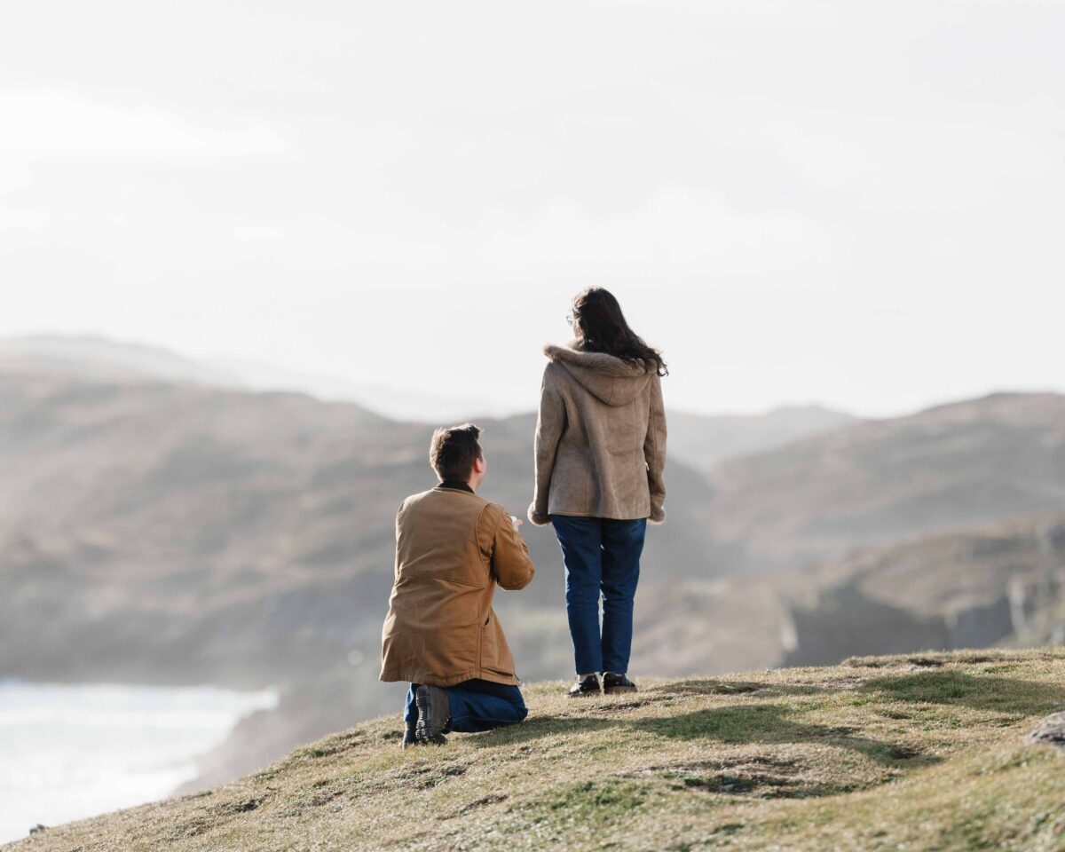 Man proposing on one knee at Baltimore Beacon in Ireland on a bright winter day