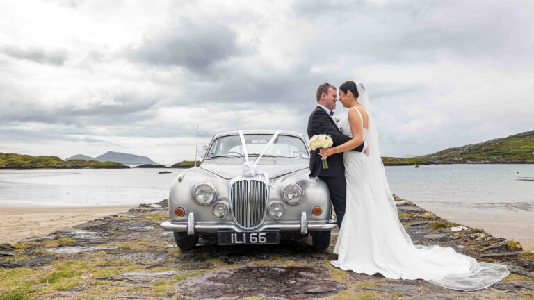 Bride and groom beside a vintage Jaguar on the shore at Waterville, Co. Kerry