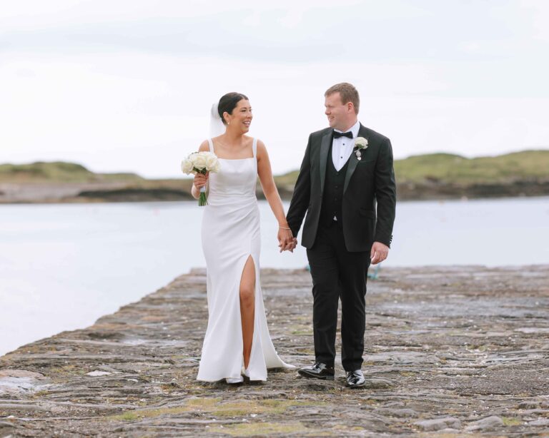 Bride and groom walking hand in hand along a stone pier by the sea, Co. Kerry wedding