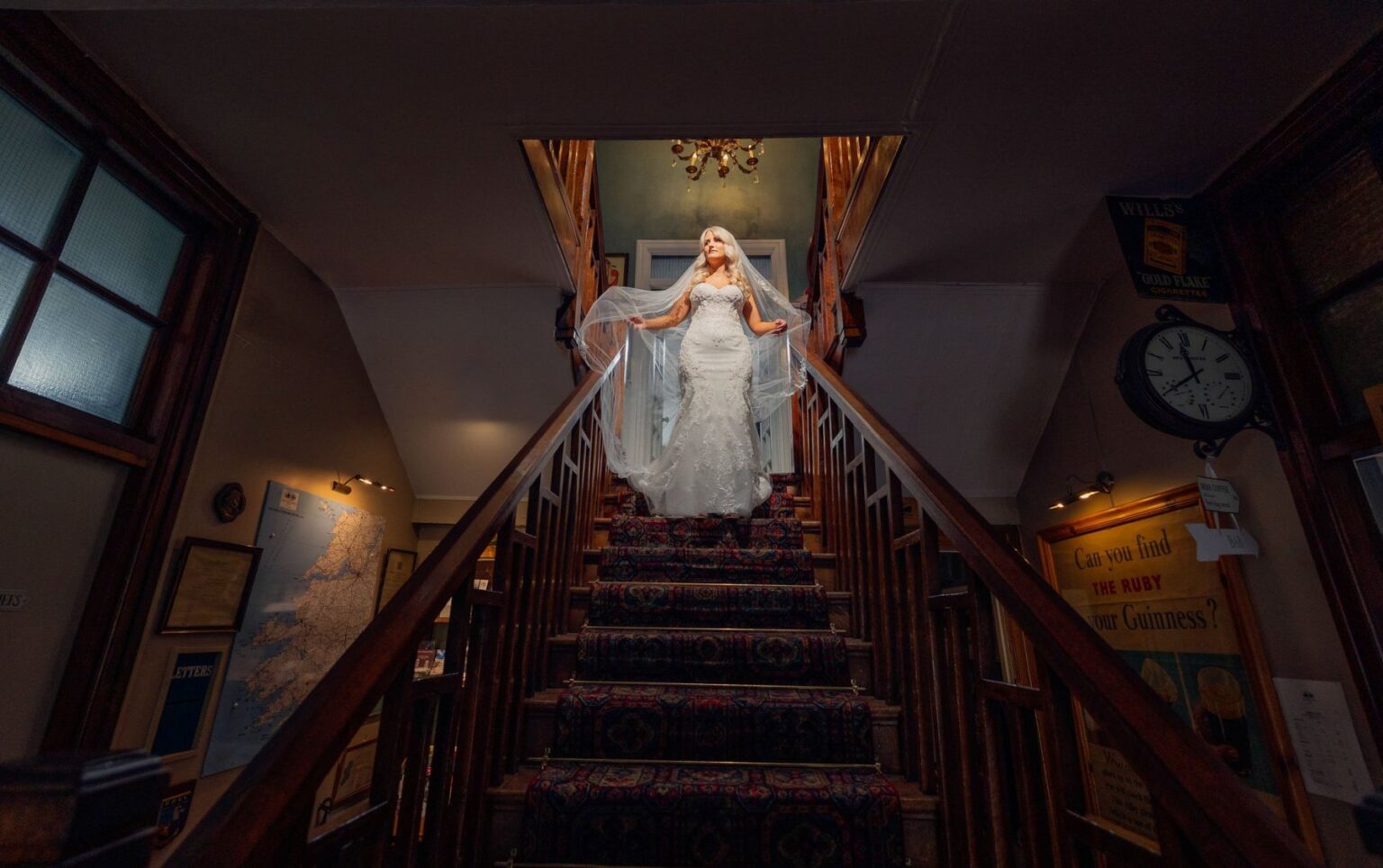 Bride in a lace wedding dress and long veil standing at the top of a carpeted staircase at Gougane Barra Hotel, West Cork