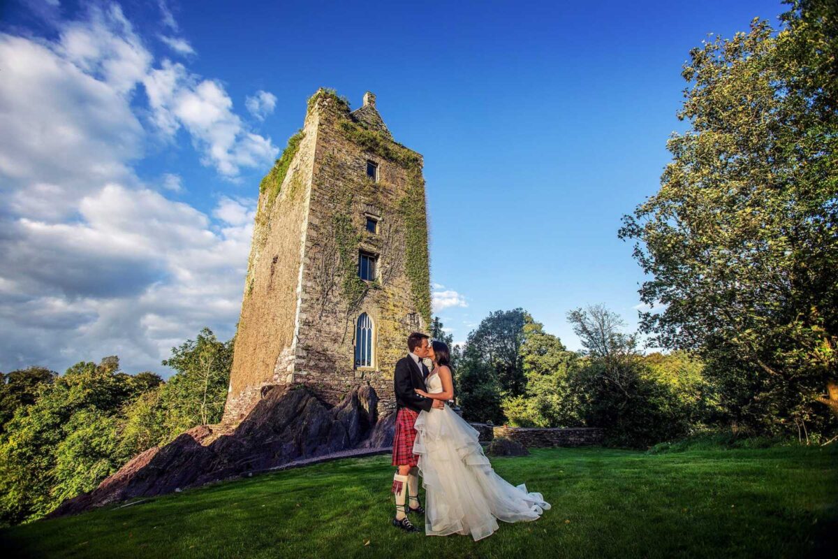 Bride and groom beside a stone tower castle on a sunny day, Ireland