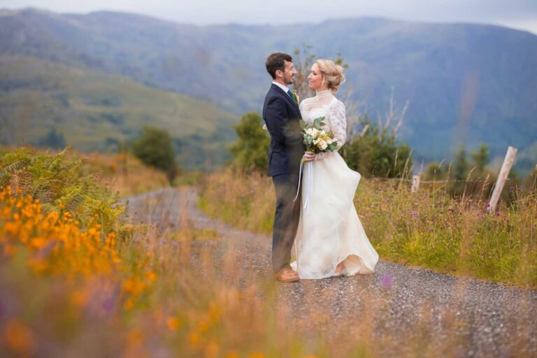Bride and groom walking a country lane through orange wildflowers in the mountains of Co. Cork