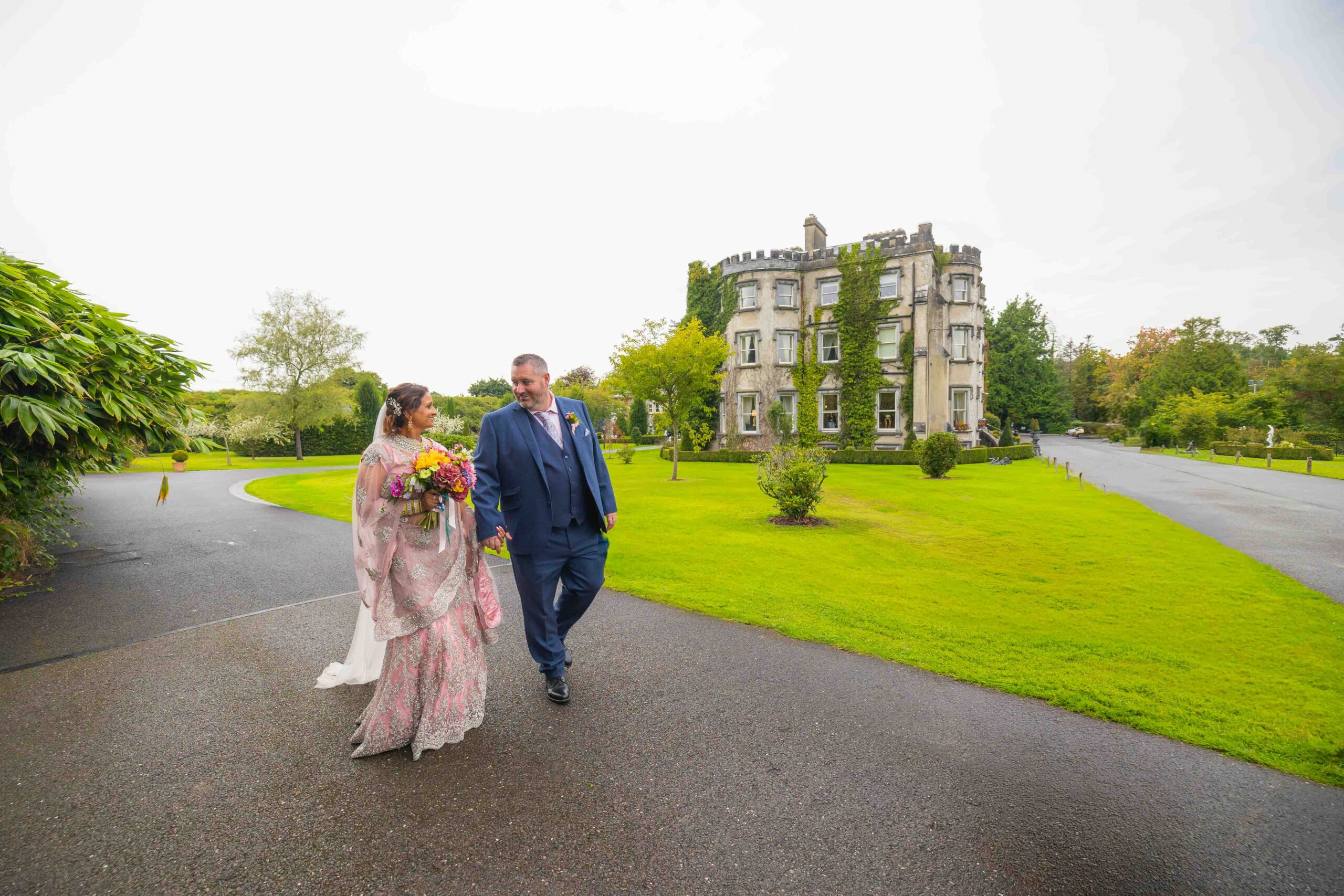 Flower girls in colourful dresses and floral halos walking down the aisle at The Belfry.