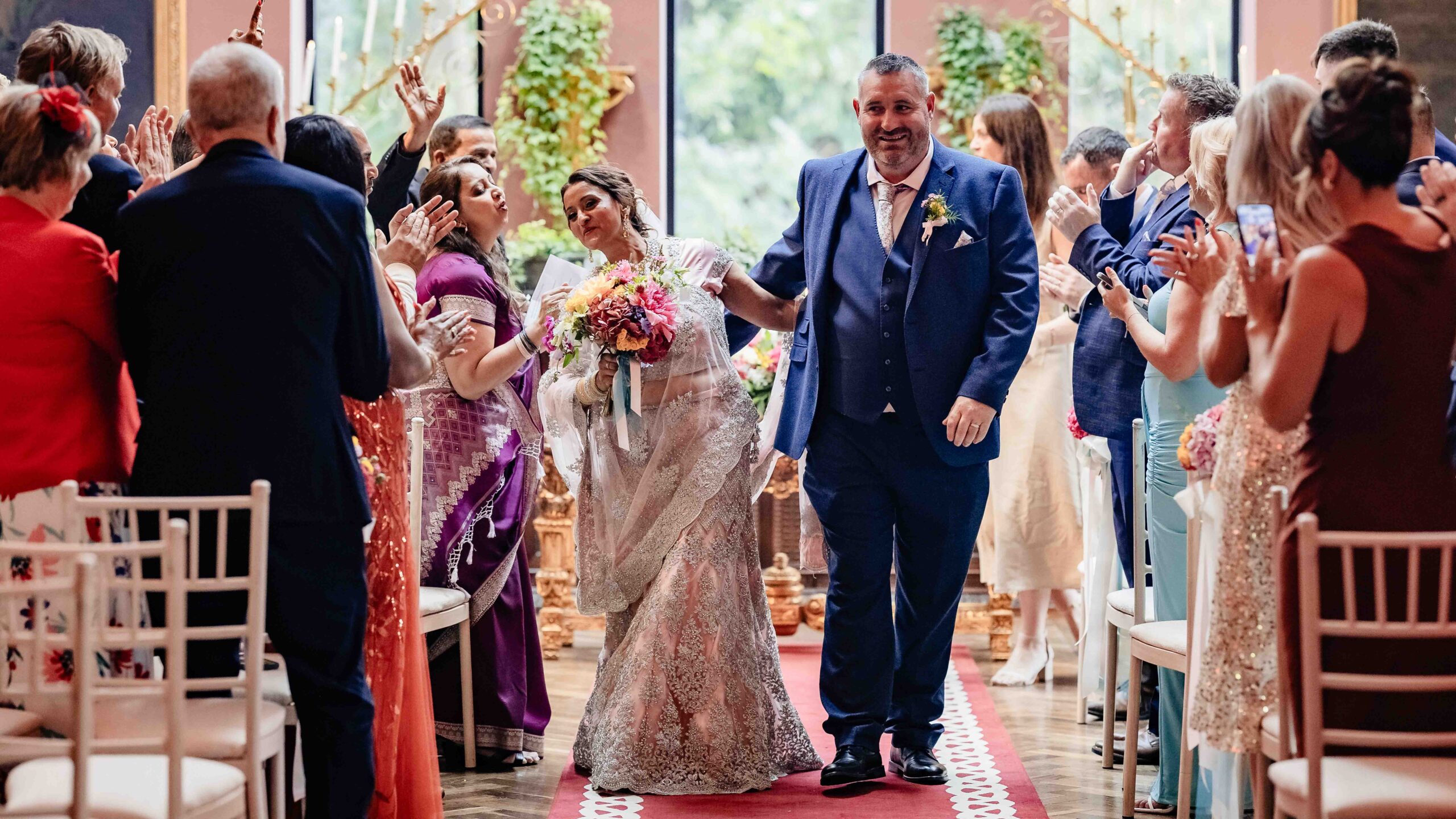 Monita's sister carrying a colourful bouquet as she walks down the aisle inside The Belfry at Ballyseede Castle.