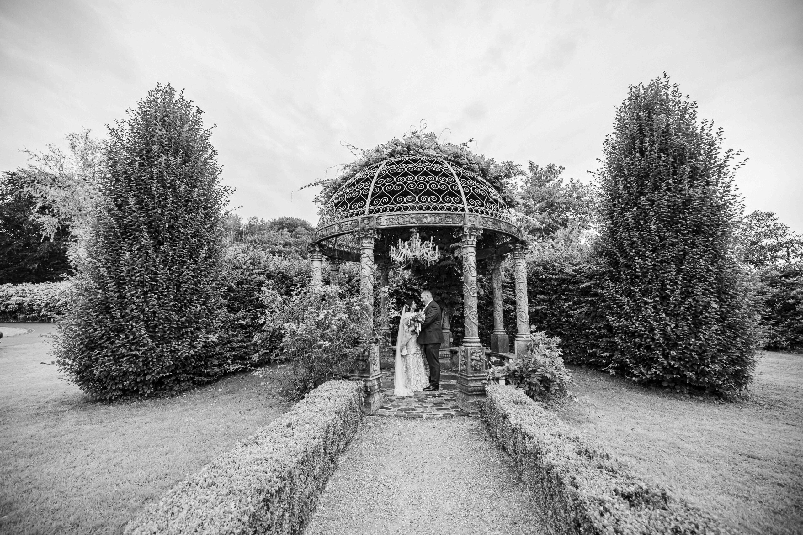 Black and white wedding portrait of Monita and Damien beneath the ornate garden gazebo at Ballyseede Castle.