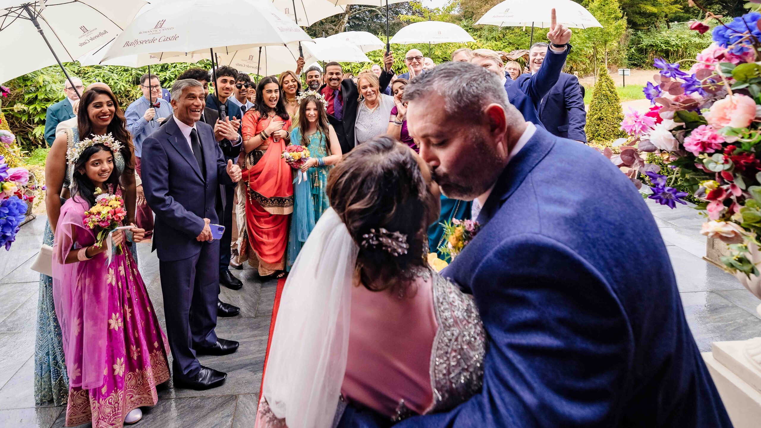 Monita and Damien walking together beneath the garden arch at Ballyseede Castle after their wedding ceremony.