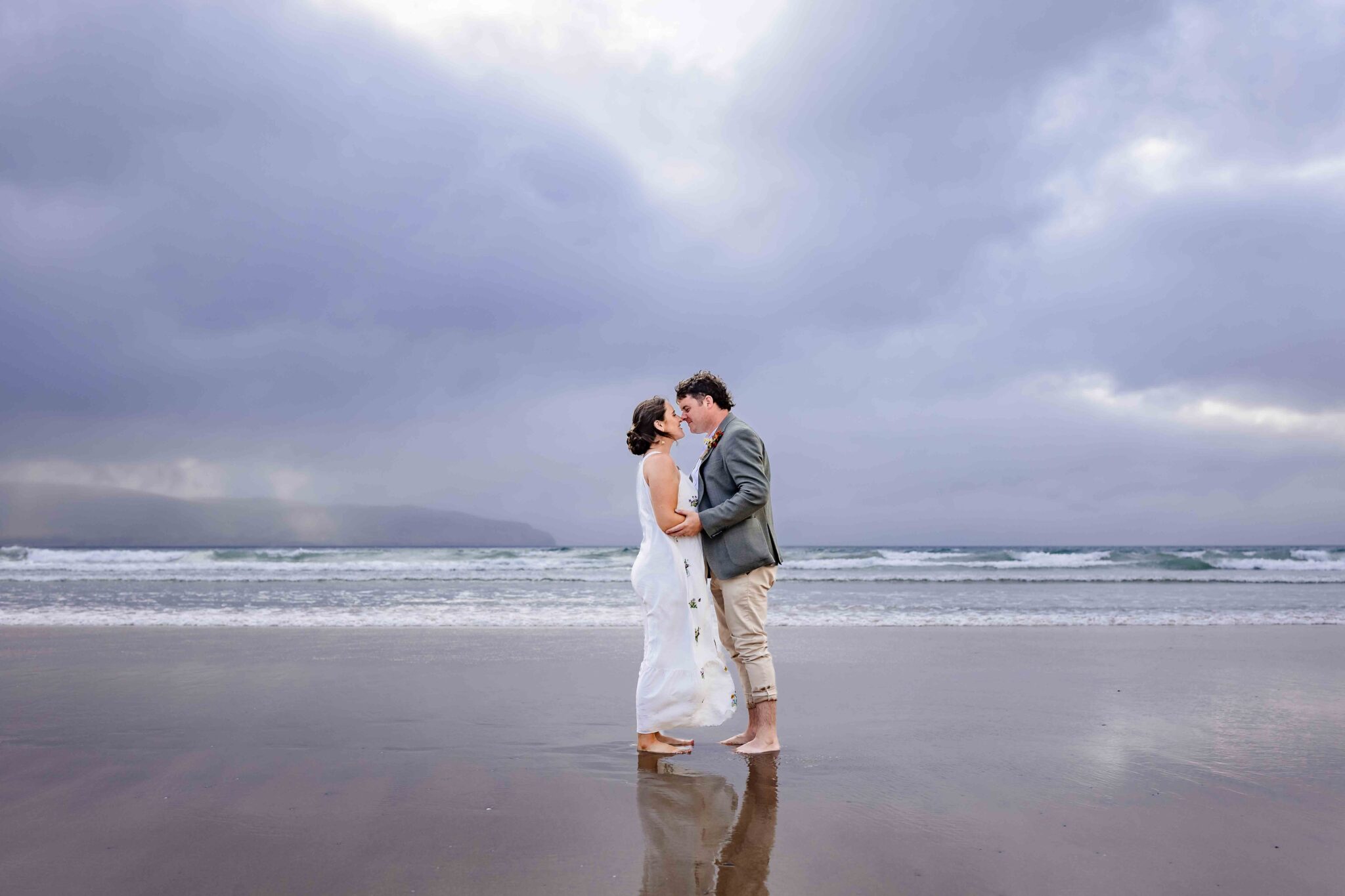 Couple embracing at the water’s edge beneath a moody sky in West Kerry