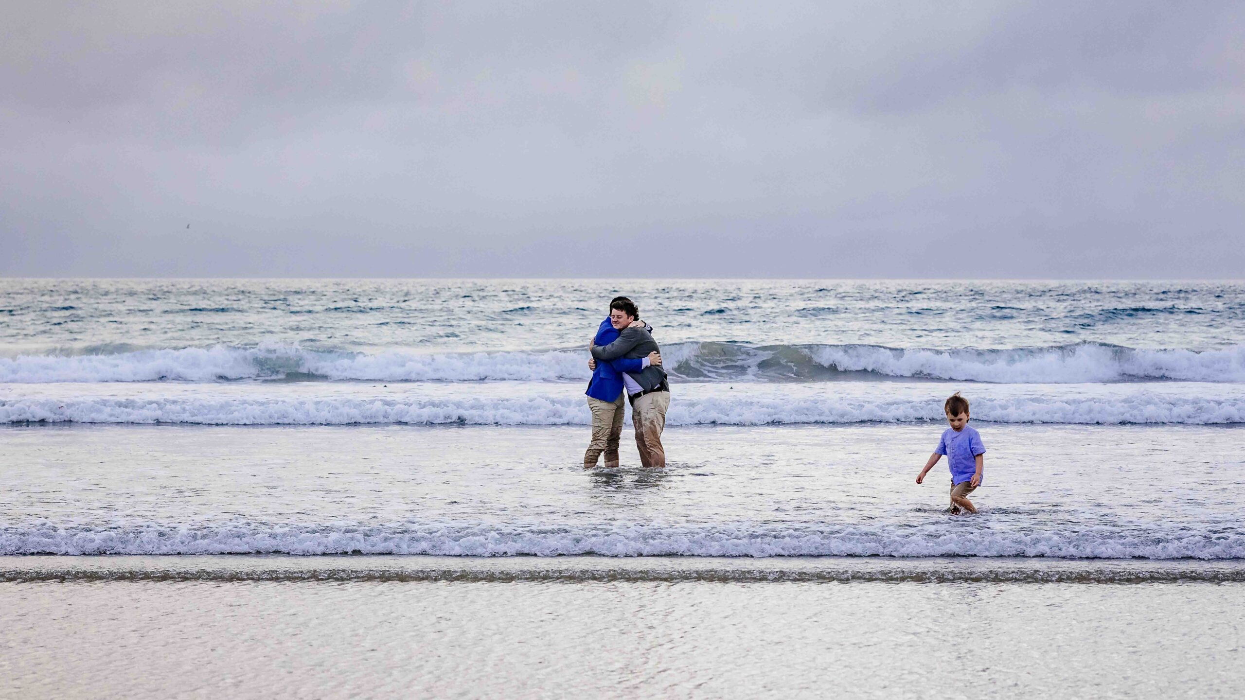 Gerard and Ciarán embracing as one of the boys plays beside them in the water
