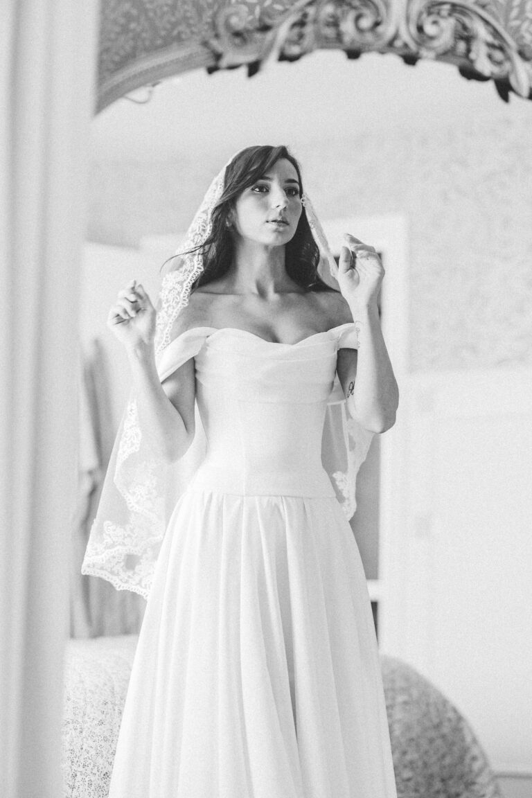 Black and white photo of the bride adjusting her off-shoulder wedding dress
