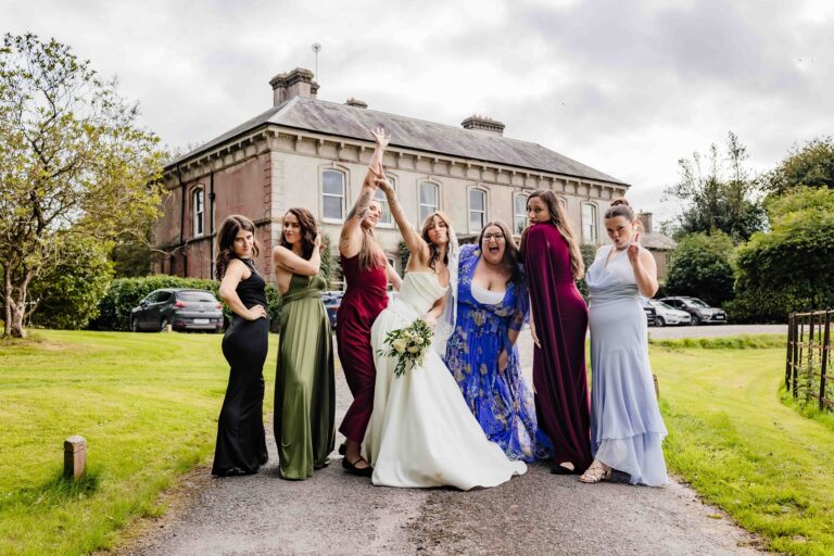 Bride and bridesmaids cheering with arms raised in front of Ballyvolane House, Cork