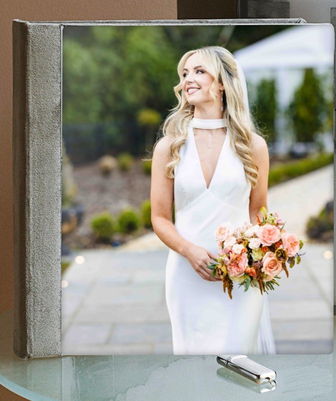 Wedding album with a crystal-clear acrylic cover showing a bride portrait, on a glass table beside a USB