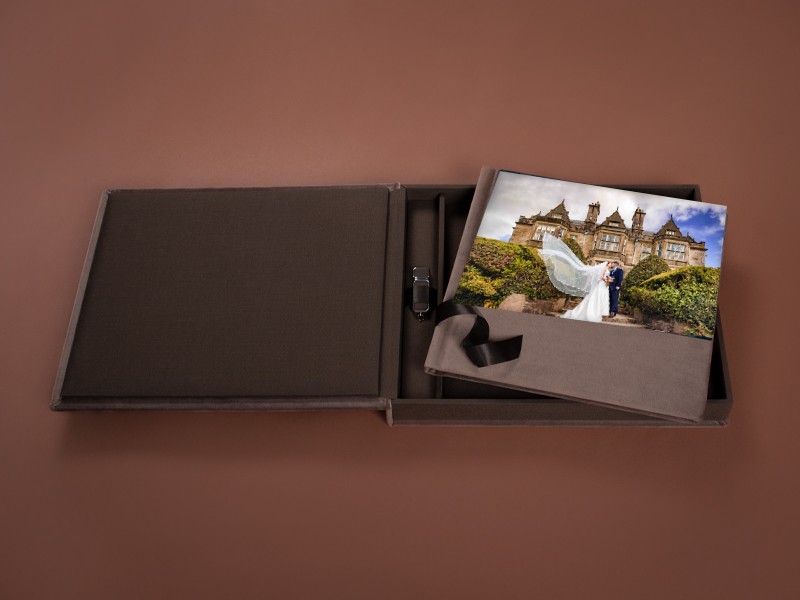 Open brown linen folio presentation box with a wedding photograph, ribbon and USB