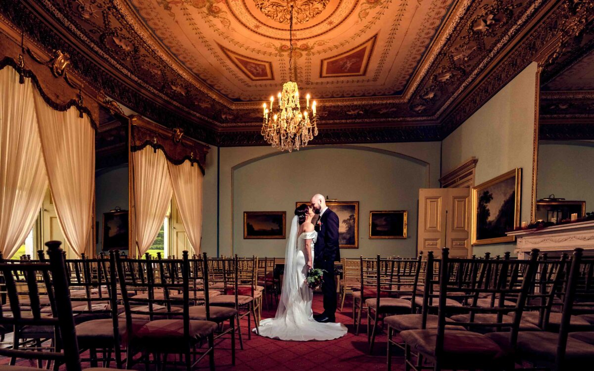 Fota House wedding photography: bride and groom kissing in the ceremony room at Fota House and Gardens, Cork, under a chandelier