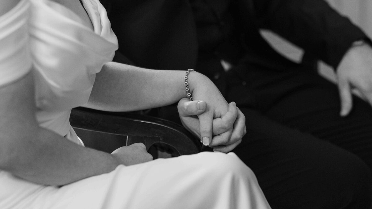 Black and white close-up of the bride's hands clasped with her partner's during the ceremony