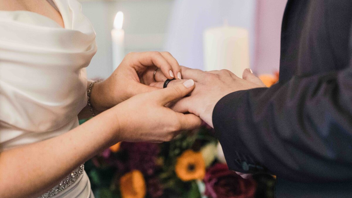 Groom slipping the wedding ring onto the bride's finger beside an autumn bouquet and candle during the ceremony