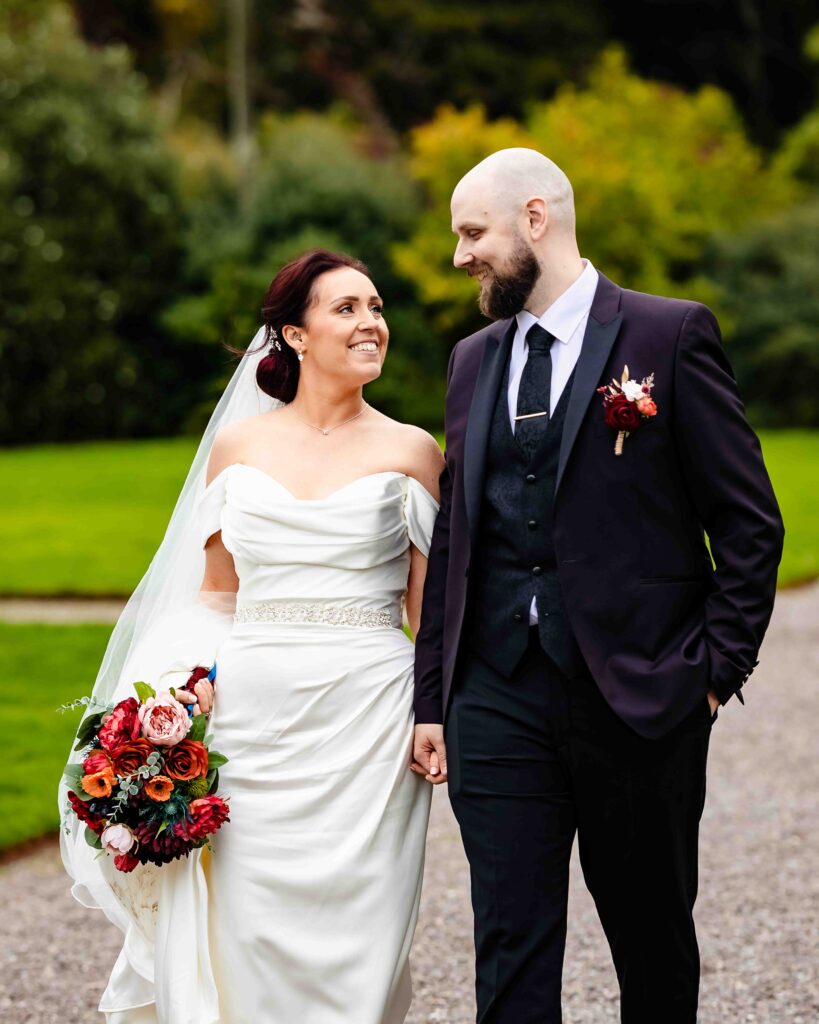 Bride and groom walking hand in hand and smiling at each other in the grounds of Fota House, Cork
