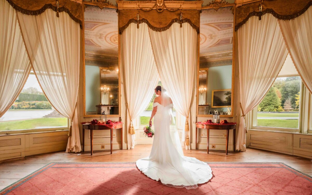 Bride standing in front of tall draped windows overlooking the grounds inside Fota House and Gardens, Cork