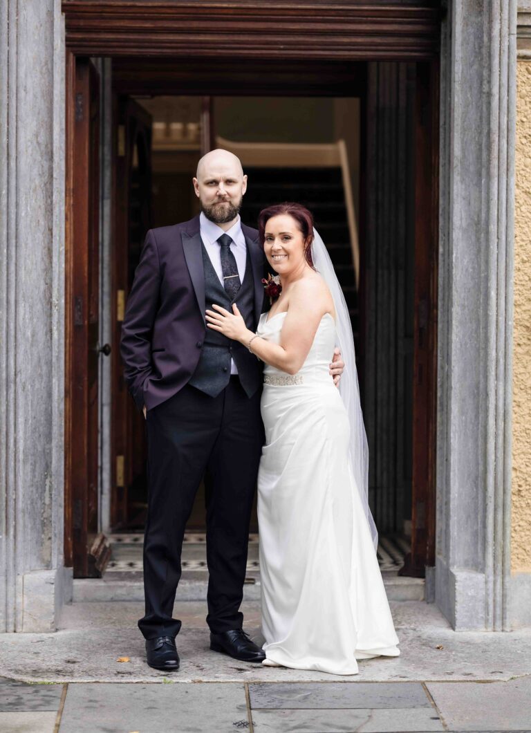 Bride and groom posing together in a grand stone doorway on their wedding day, Cork