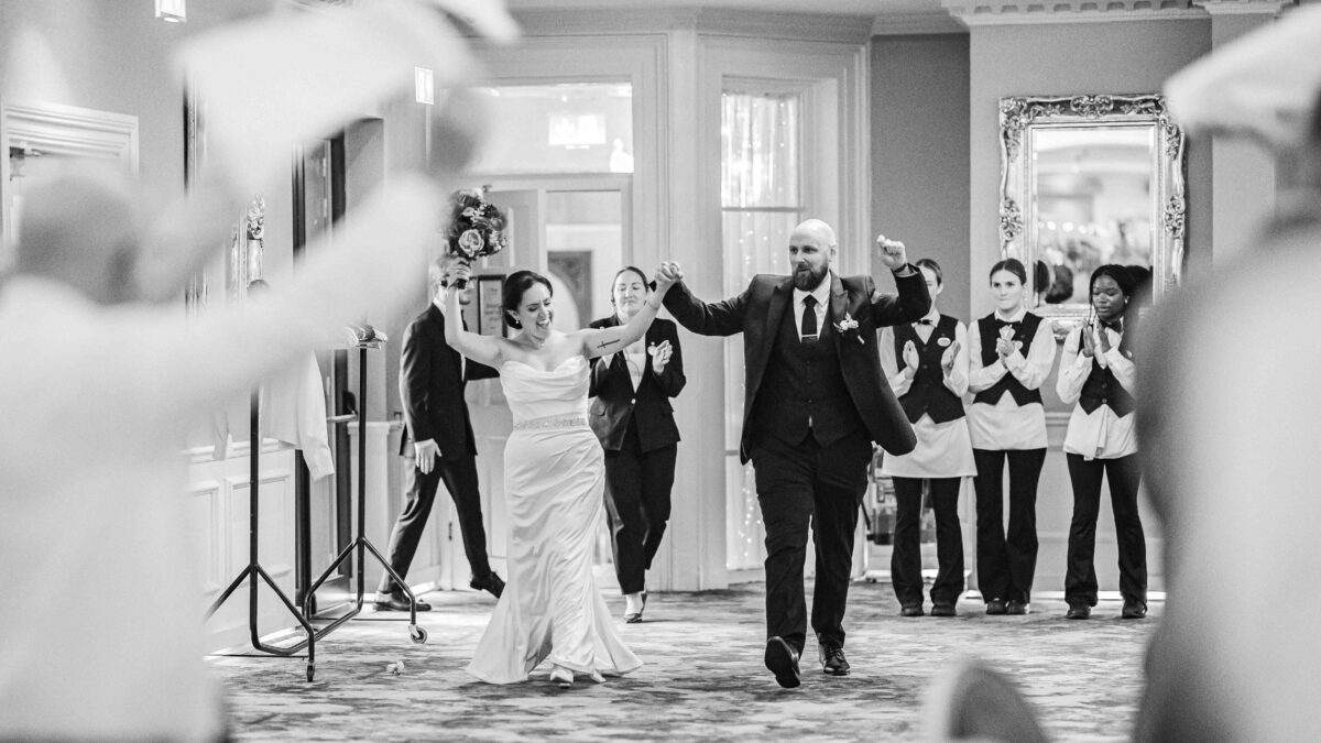 Black and white photo of the bride and groom walking into the wedding reception to cheering guests and staff, Vienna Woods Hotel, Cork