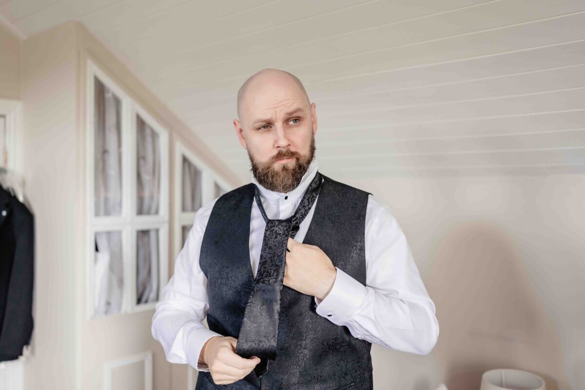 Groom in a black patterned waistcoat adjusting his tie while getting ready