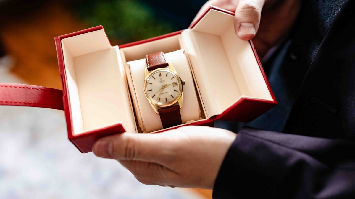 Gold wristwatch held open in a red presentation box on the wedding morning