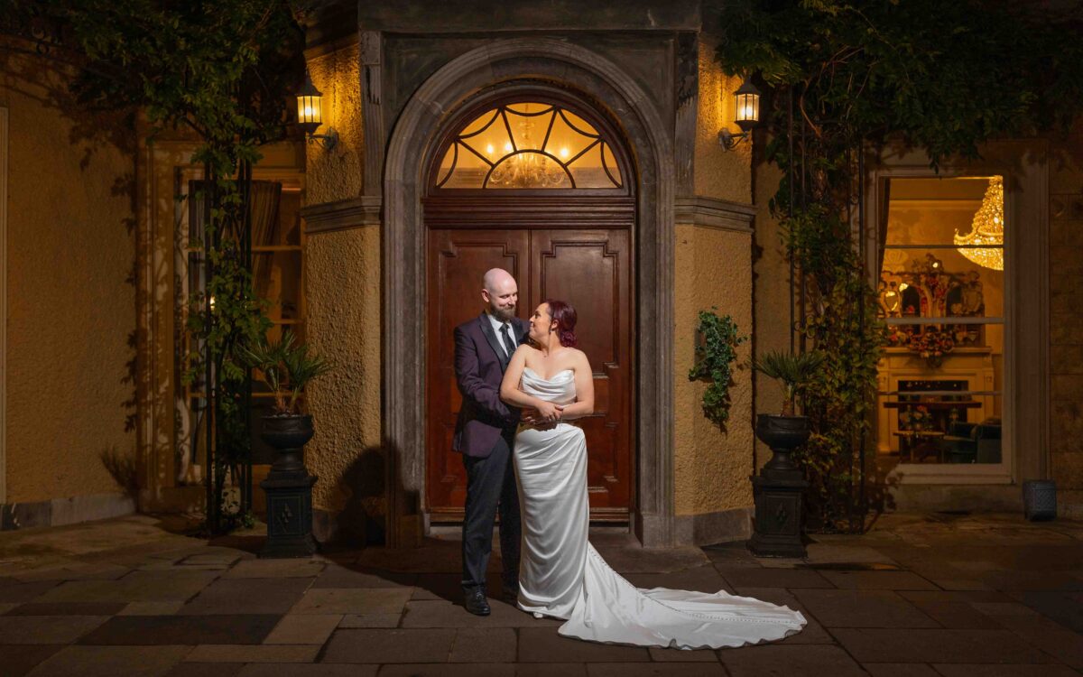 Dave with his arm around Sinéad beside the arched front door at night, Vienna Woods Hotel wedding, Cork