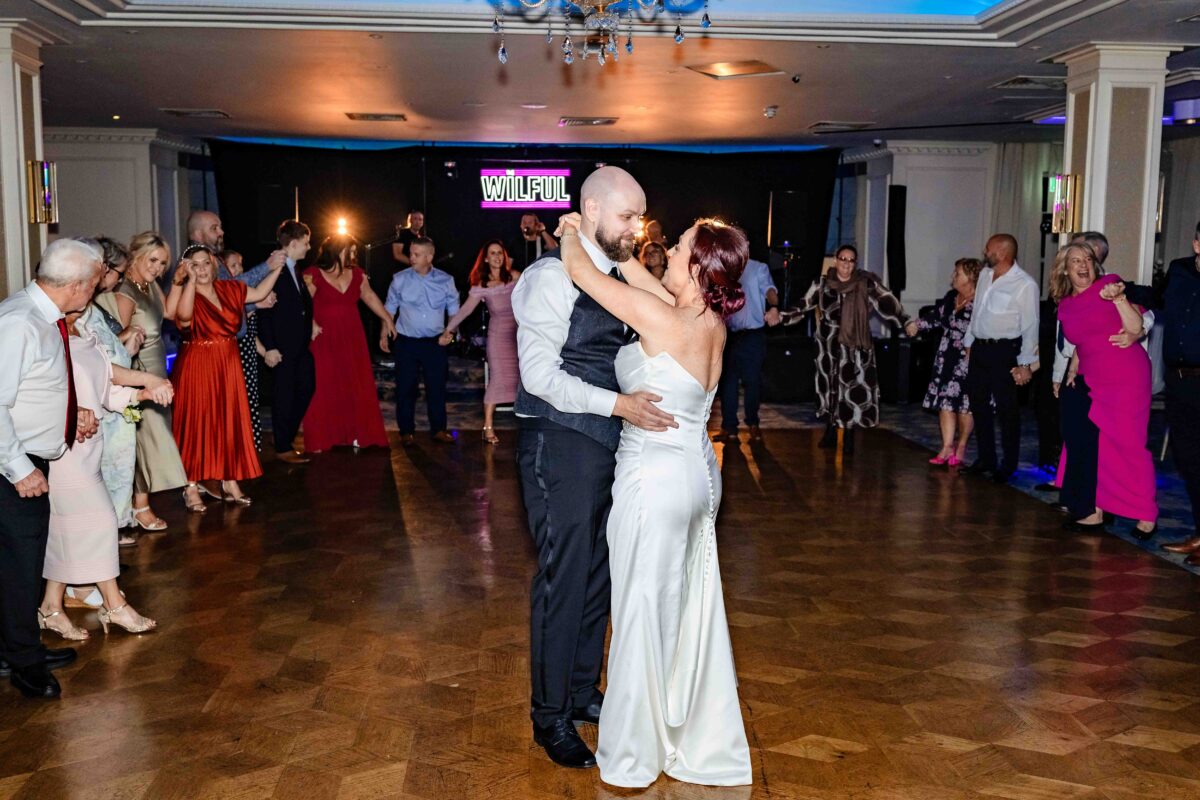 Bride and groom dancing their first dance on the wooden dance floor with the band playing behind them